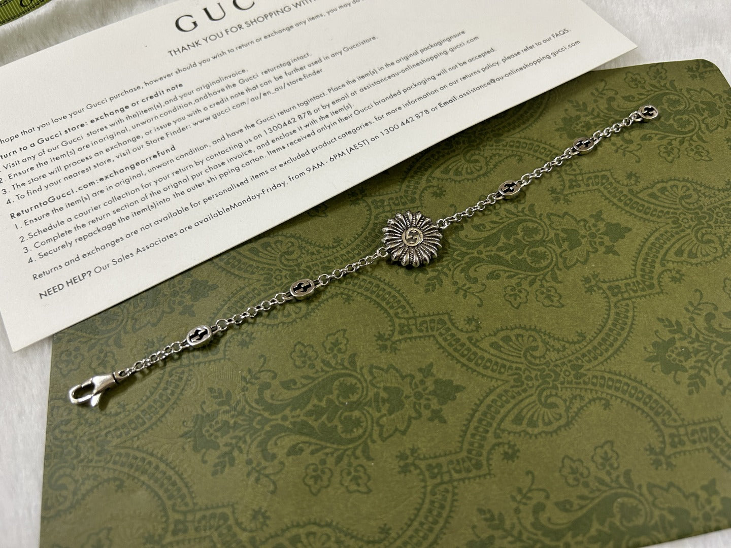Silver charm bracelet with turquoise flower medallion and oval logo chain links.