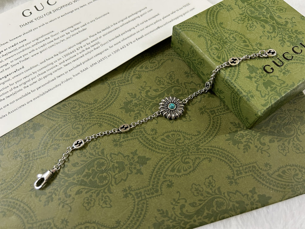 Silver link bracelet with turquoise flower charm, clasp end, and logo medallions.