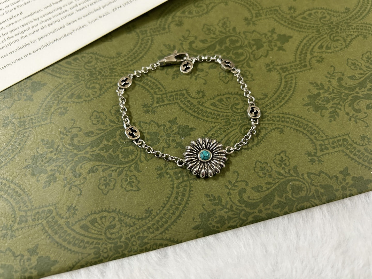 Silver charm bracelet with turquoise flower center and oval logo link pattern.