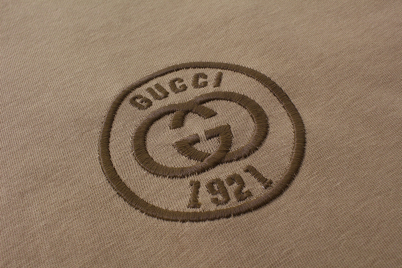 Close-up of Gucci 1971 crest logo patch on tan T-shirt