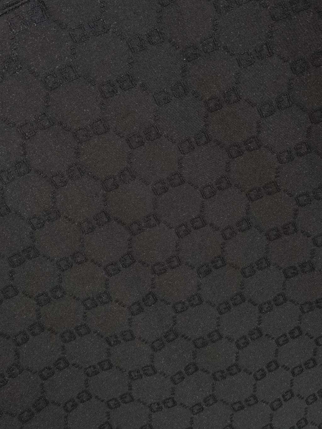 Gucci polo shirt fabric close-up, black textured interlocking pattern