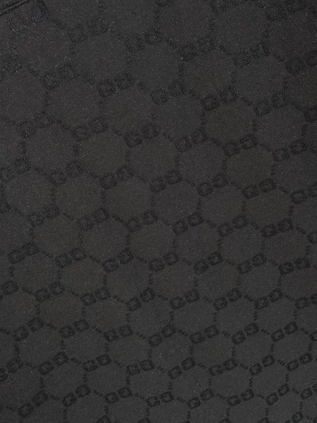 Gucci polo shirt fabric close-up, black textured interlocking pattern