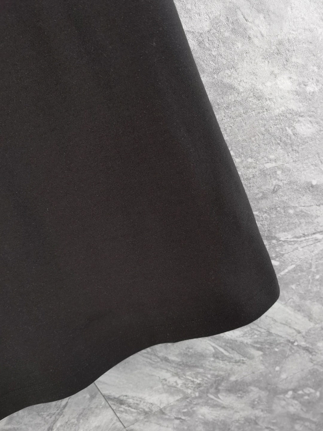 Black polo shirt hem area with smooth fabric and subtle monogram pattern