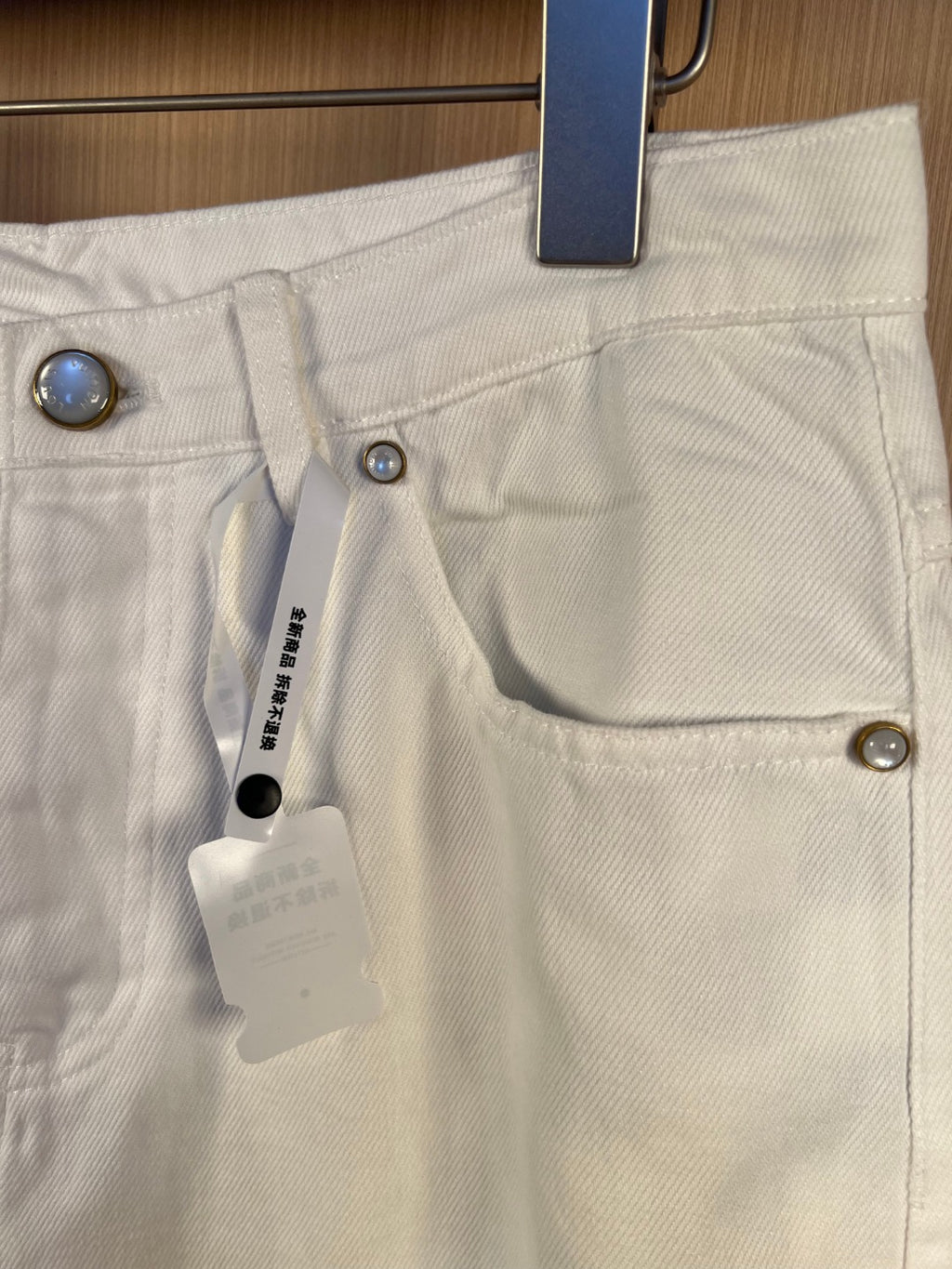 White denim pants close-up of front pockets and metal buttons