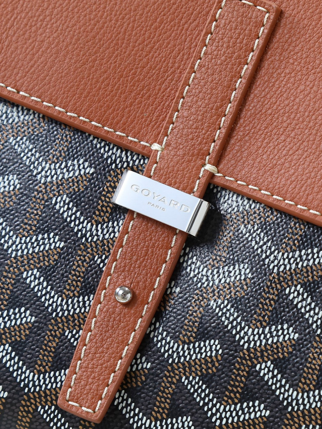 Goyard bag strap detail with brown leather trim and silver-toned clasp on canvas.