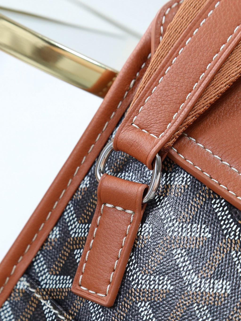 Goyard bag strap hardware with brown leather loop and stitched edges on canvas.