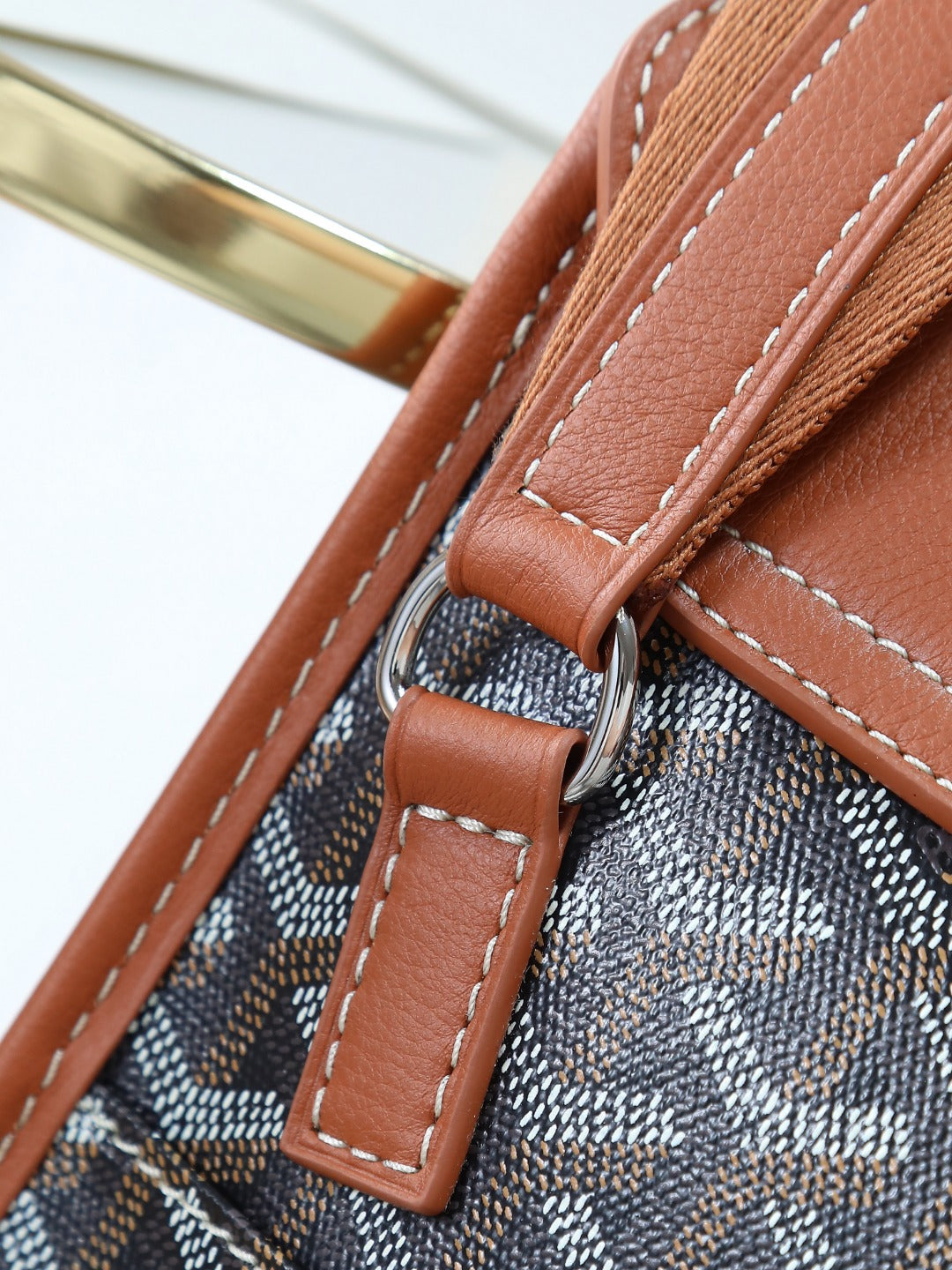 Goyard bag strap hardware with brown leather loop and stitched edges on canvas.