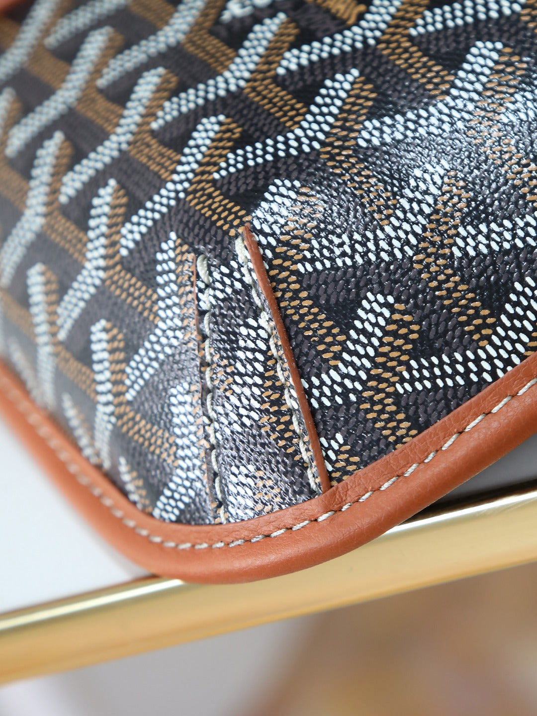 Goyard bag corner with brown leather piping and stitched monogram fabric close-up.