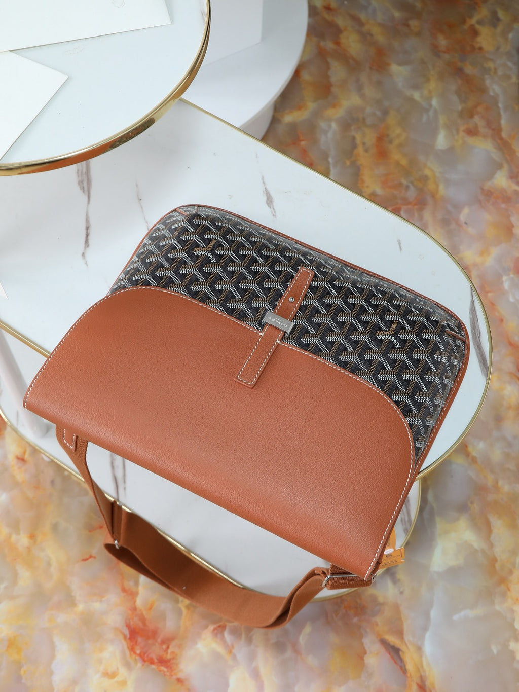 Goyard bag top view with brown leather flap, gray monogram canvas, and short strap.