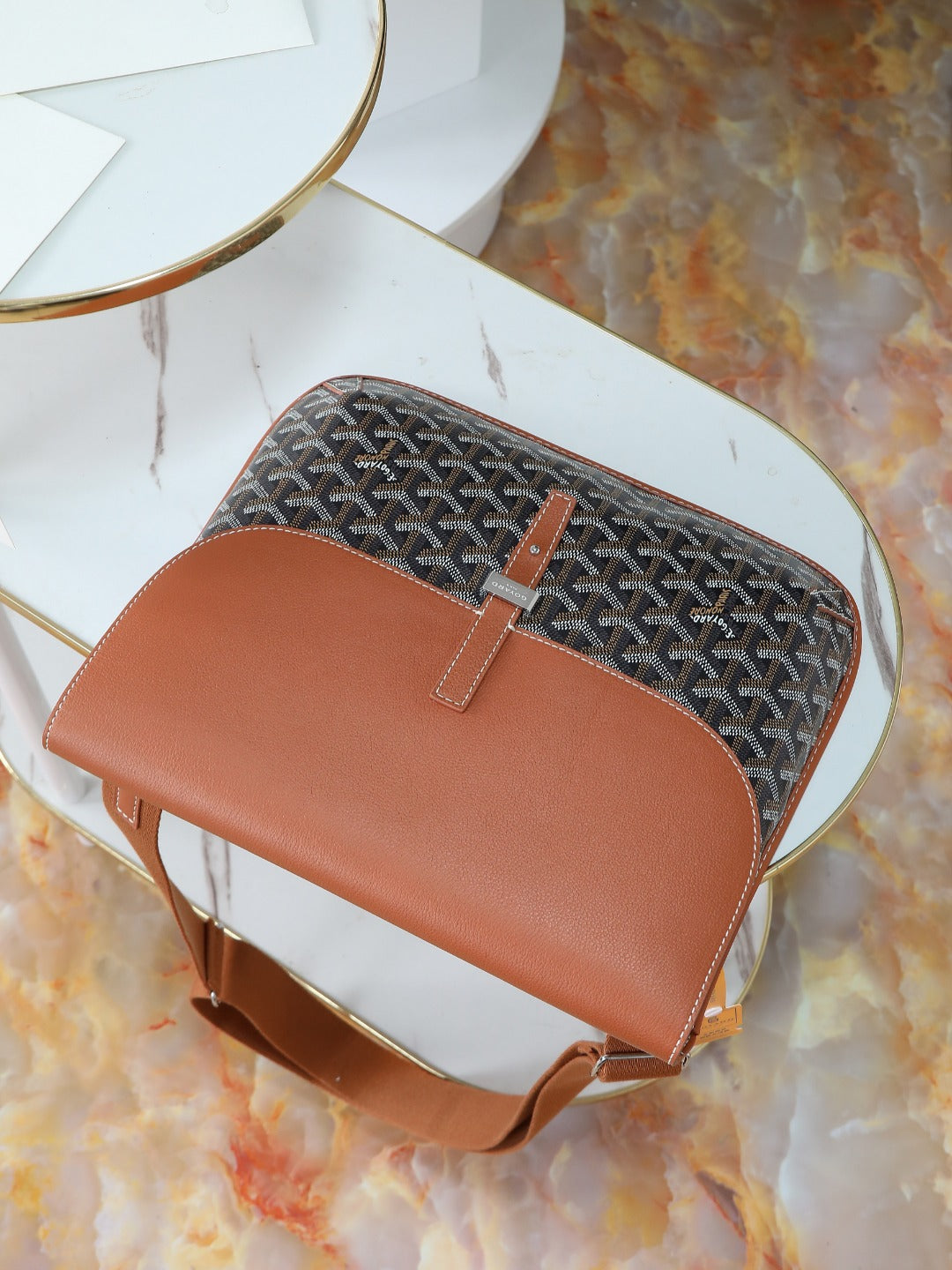 Goyard bag top view with brown leather flap, gray monogram canvas, and short strap.