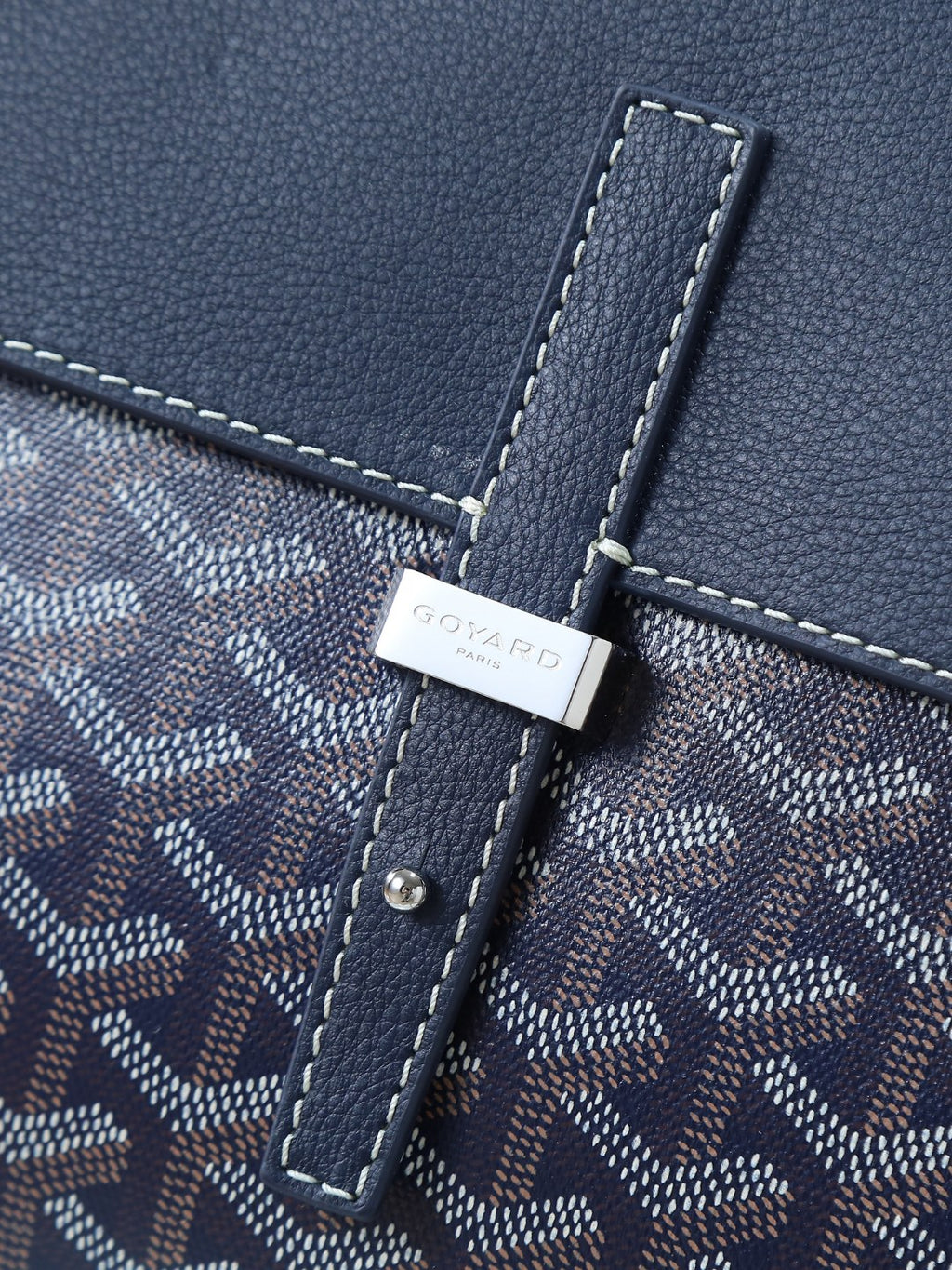 Goyard crossbody bag detail: dark blue monogram canvas with stitched trim and tag