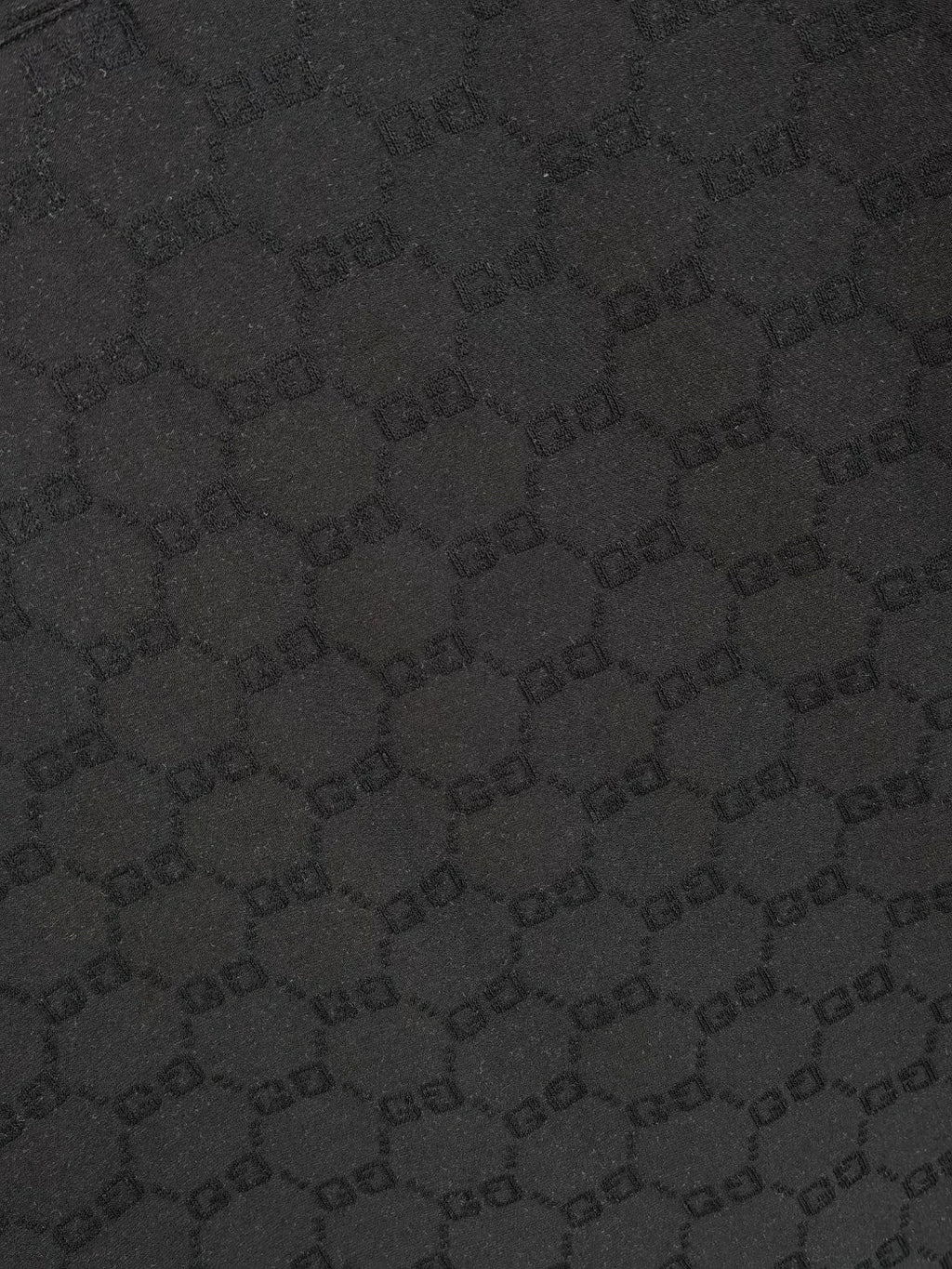 Black Gucci polo shirt fabric close-up showing repeating GG monogram pattern