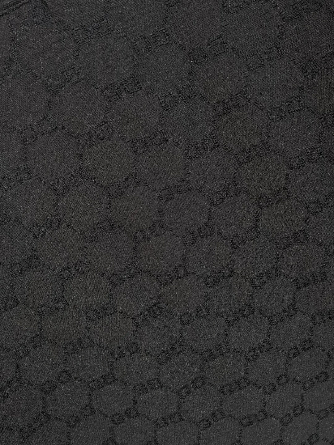 Black Gucci polo shirt fabric close-up showing repeating GG monogram pattern