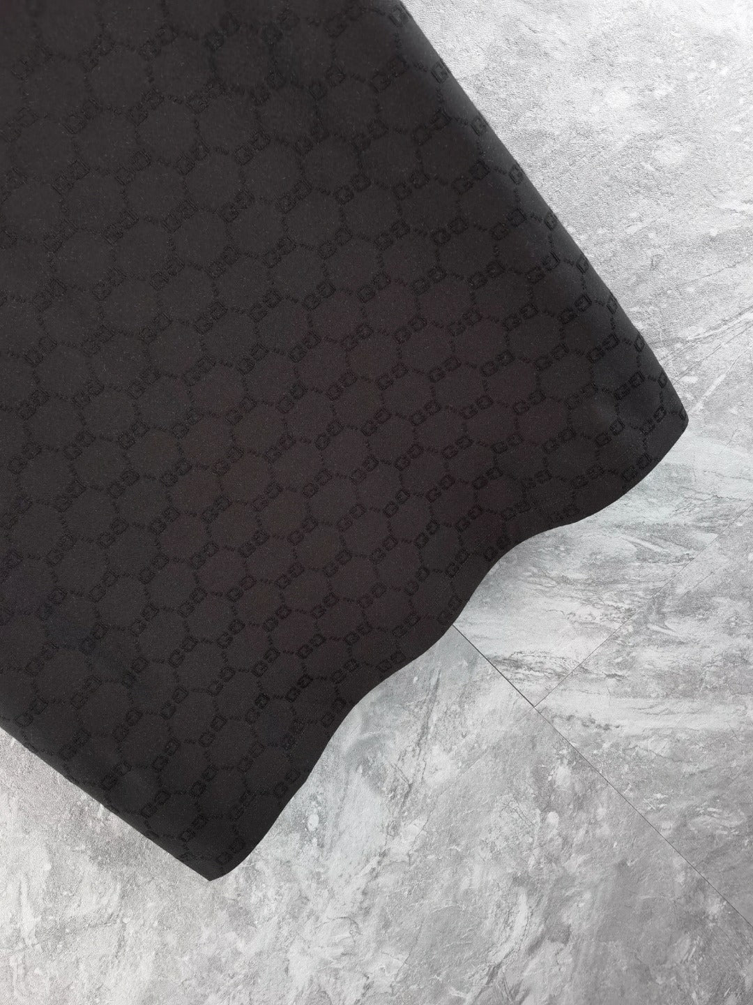Black Gucci polo shirt fabric detail with repeating monogram pattern
