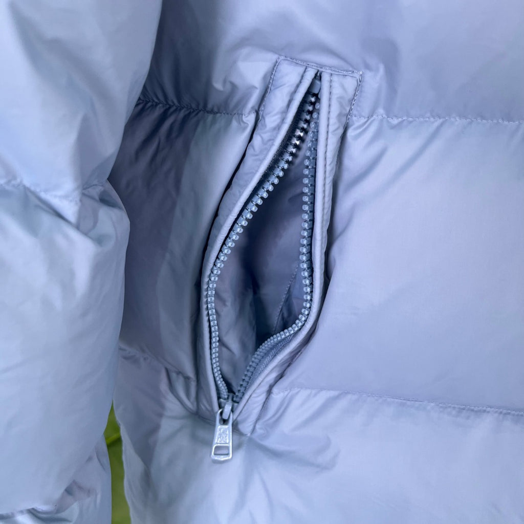 Light blue puffer jacket close-up with curved zip pocket opening