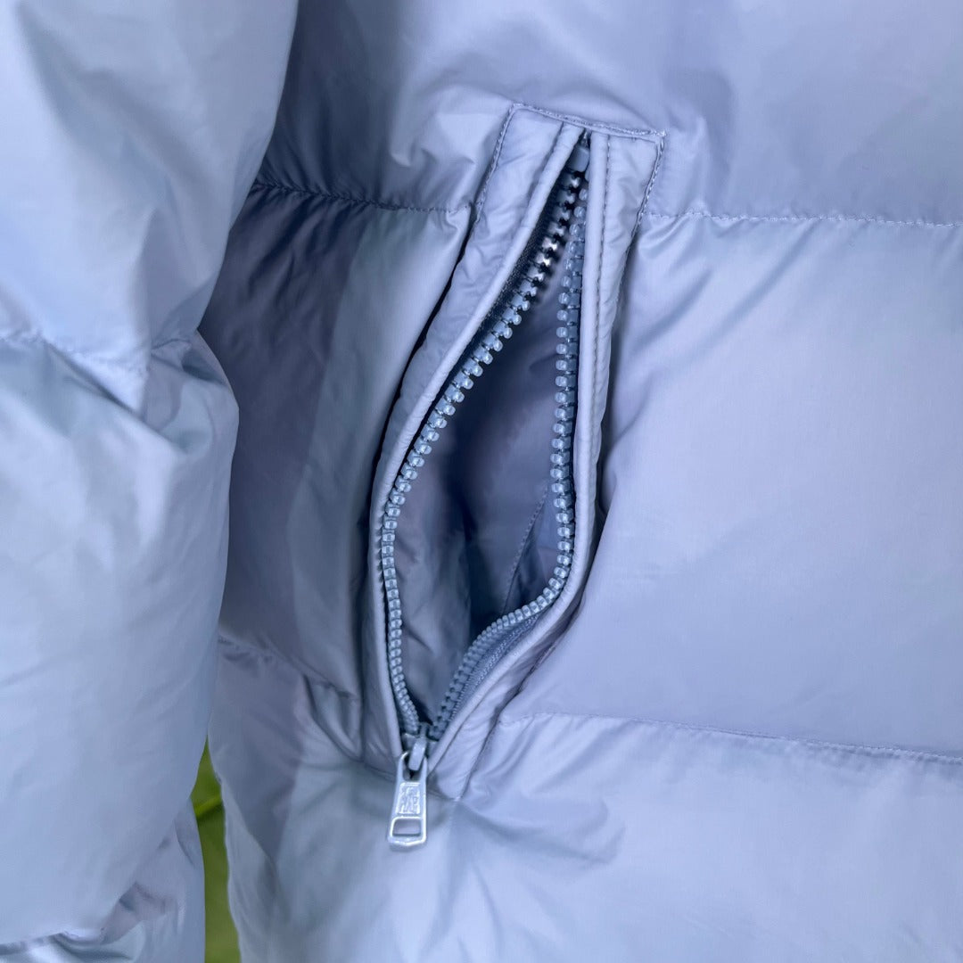 Light blue puffer jacket close-up with curved zip pocket opening