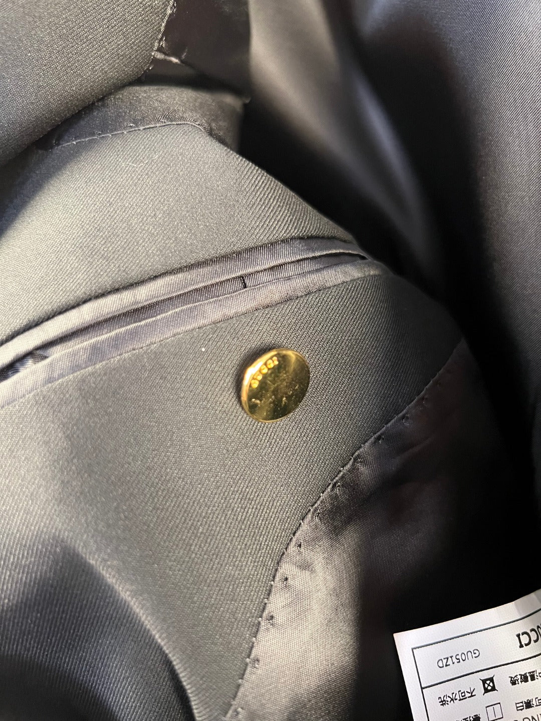 Dark blazer pocket with gold-tone button and stitched trim