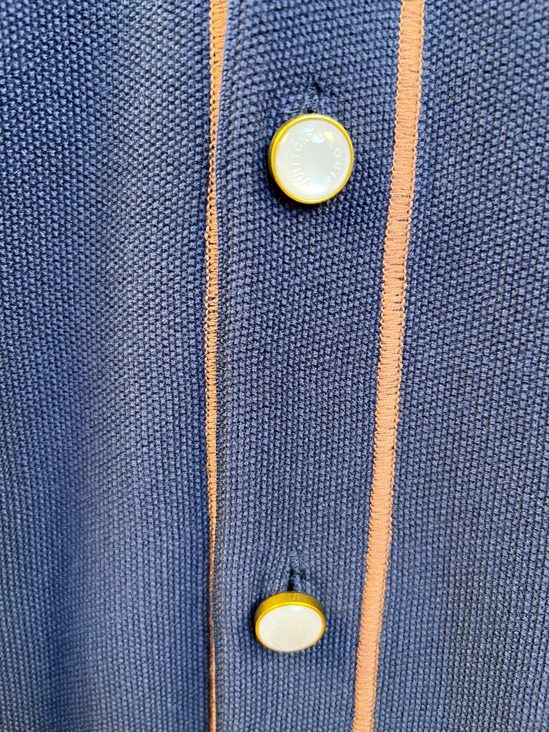 Navy knit polo shirt with tan-and-coral trim and gold button accents