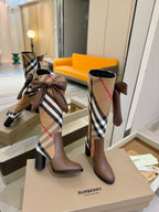 Brown heeled boots with Burberry check shaft and bow, standing on a display box