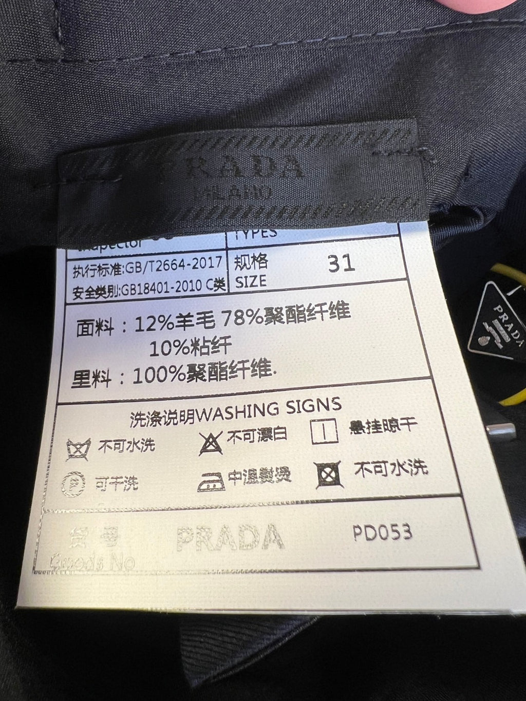 Prada fabric care label on navy pants with washing instructions.