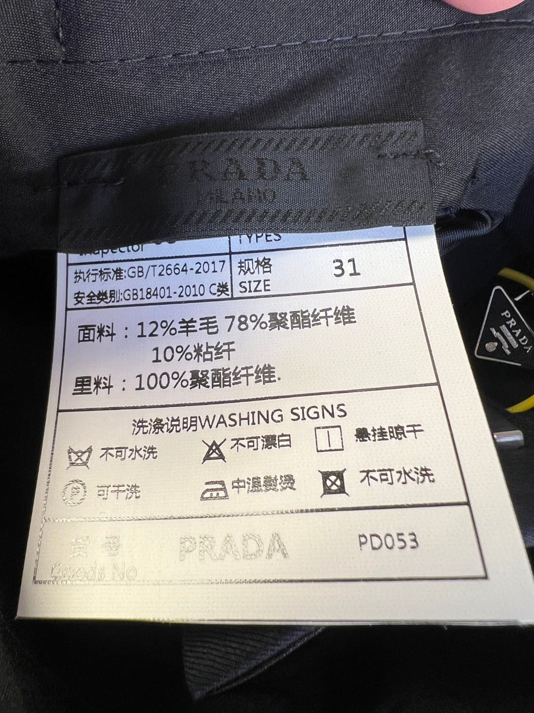Prada fabric care label on navy pants with washing instructions.