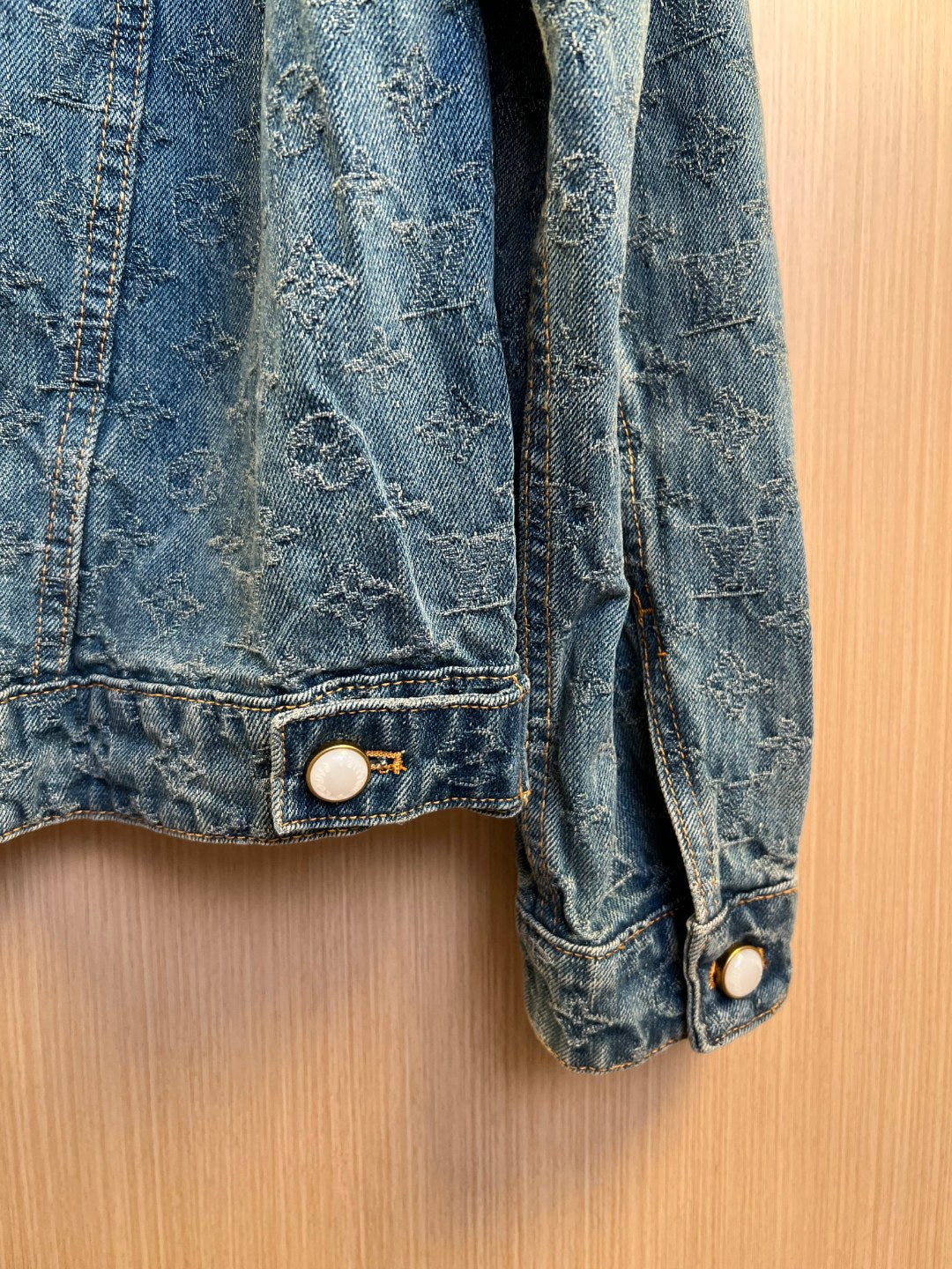 Denim jacket sleeve cuff with stitched hem and round metal button.