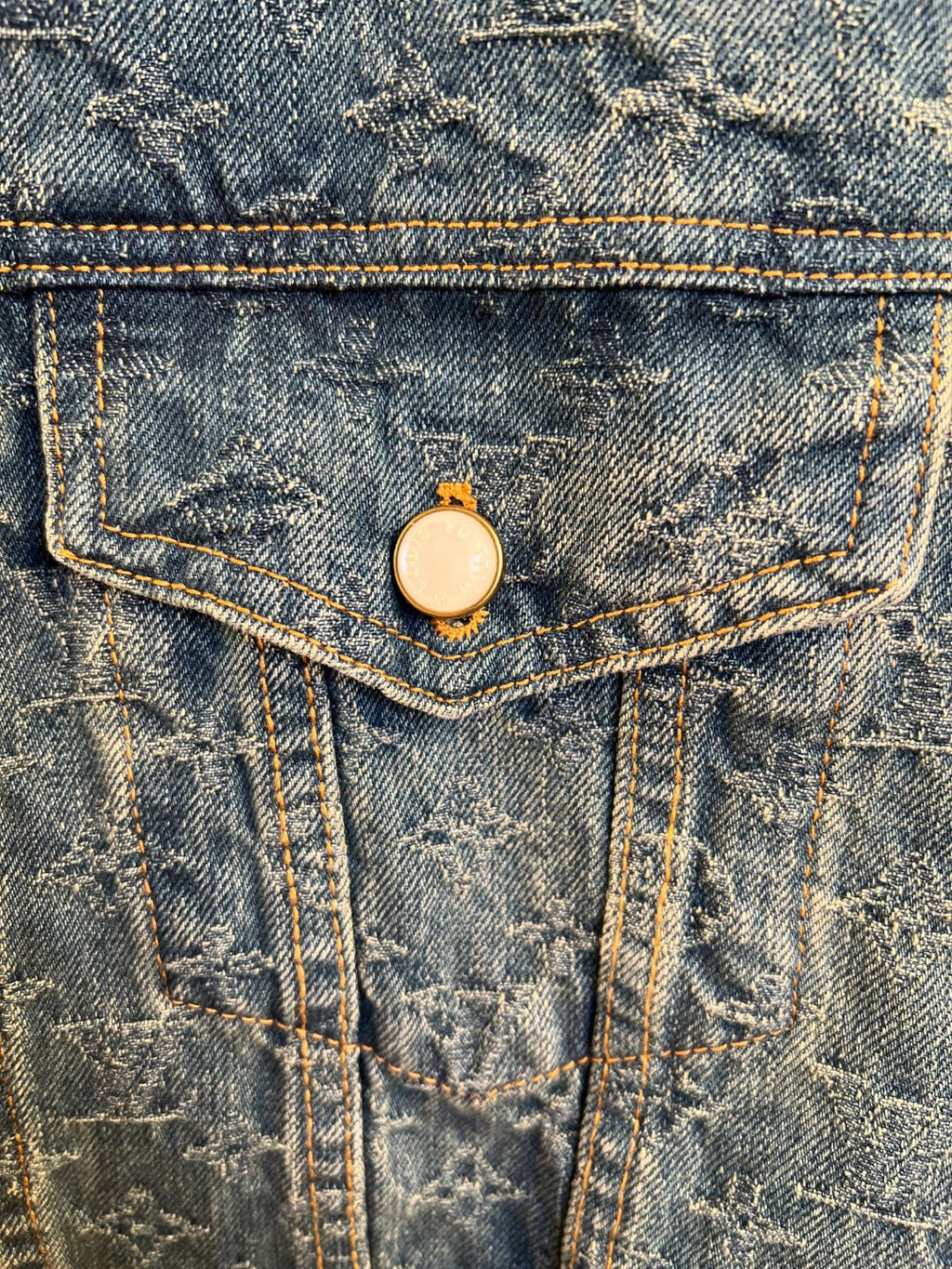 Denim jacket front flap pocket with round metal button closure.