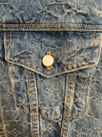 Denim jacket front flap pocket with round metal button closure.