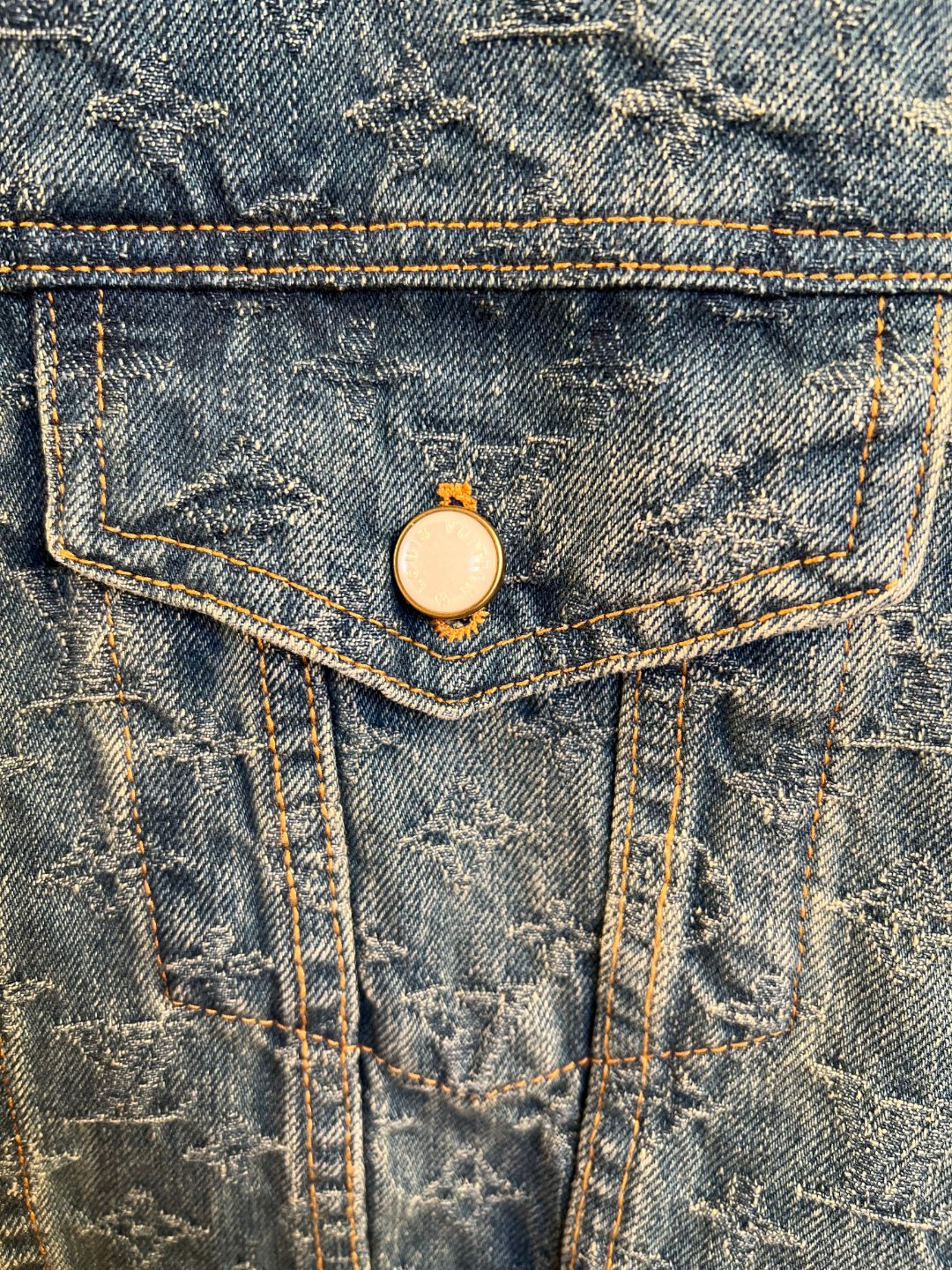 Denim jacket front flap pocket with round metal button closure.