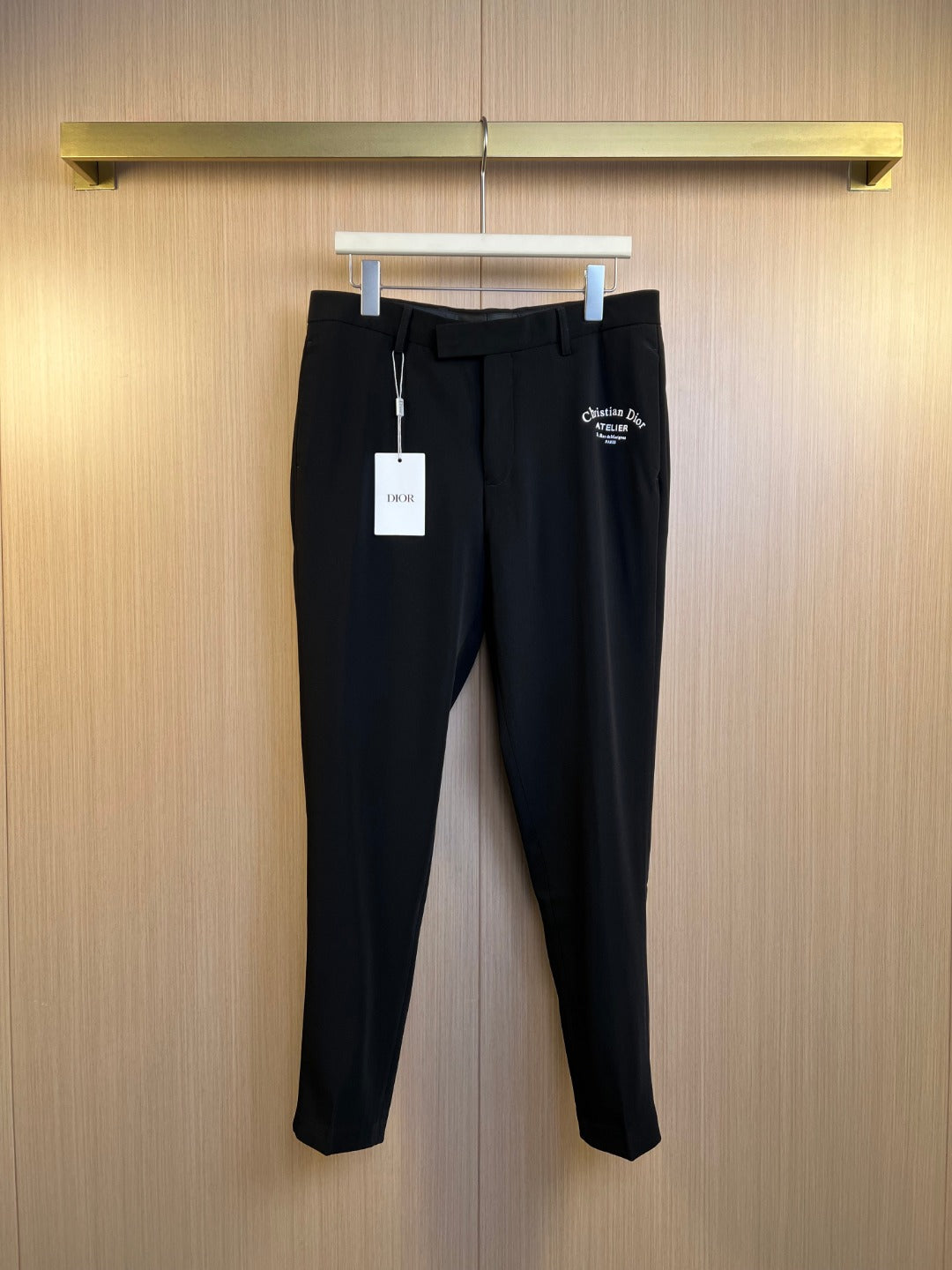 Black Dior trousers with belt loops, front zip fly, and brand tag on hanger