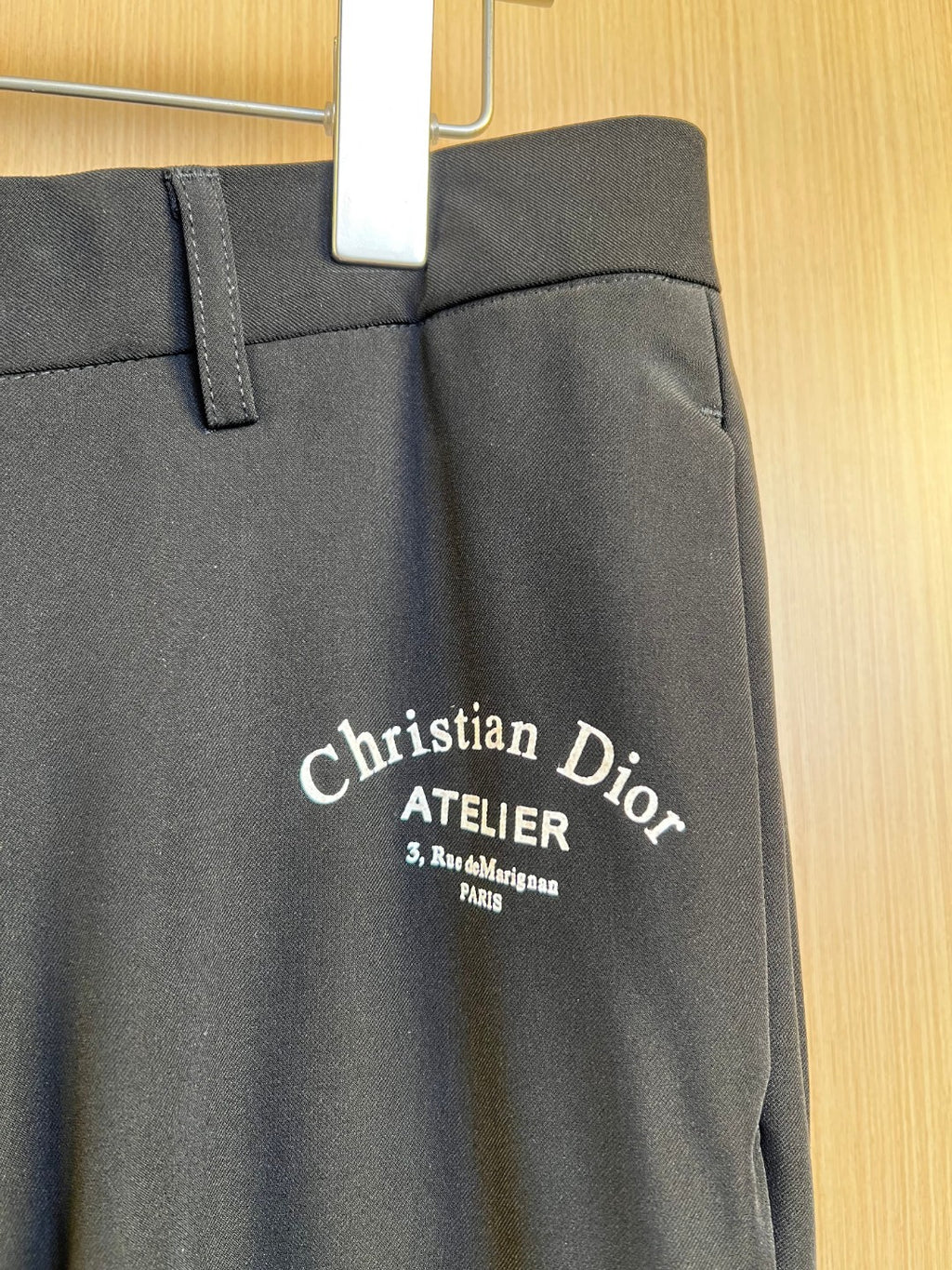 Dark pants with Christian Dior Atelier logo on front, waistband and button visible
