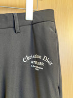 Dark pants with Christian Dior Atelier logo on front, waistband and button visible