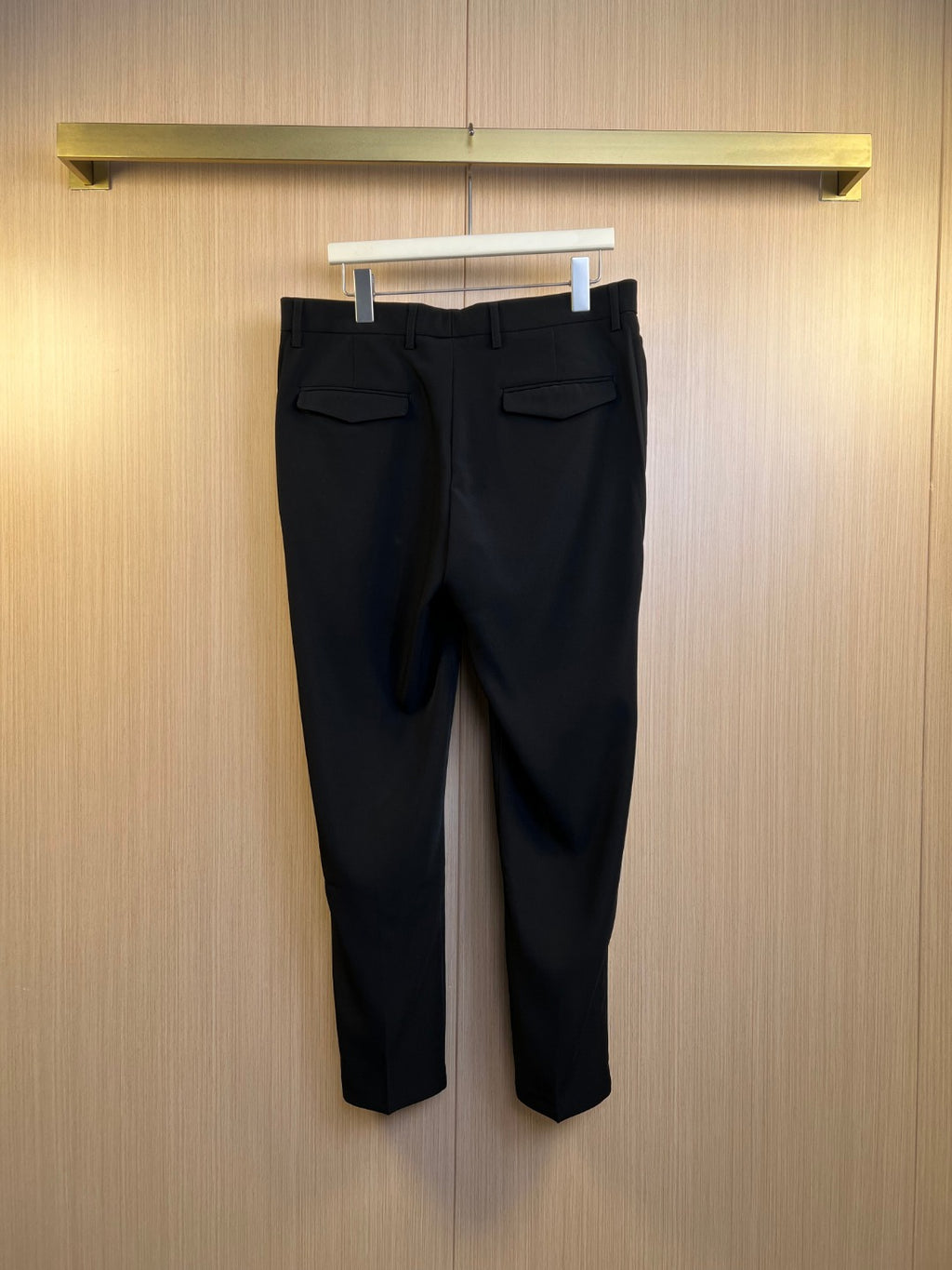 Black Dior trousers with front pockets and belt loops hanging on a display rack