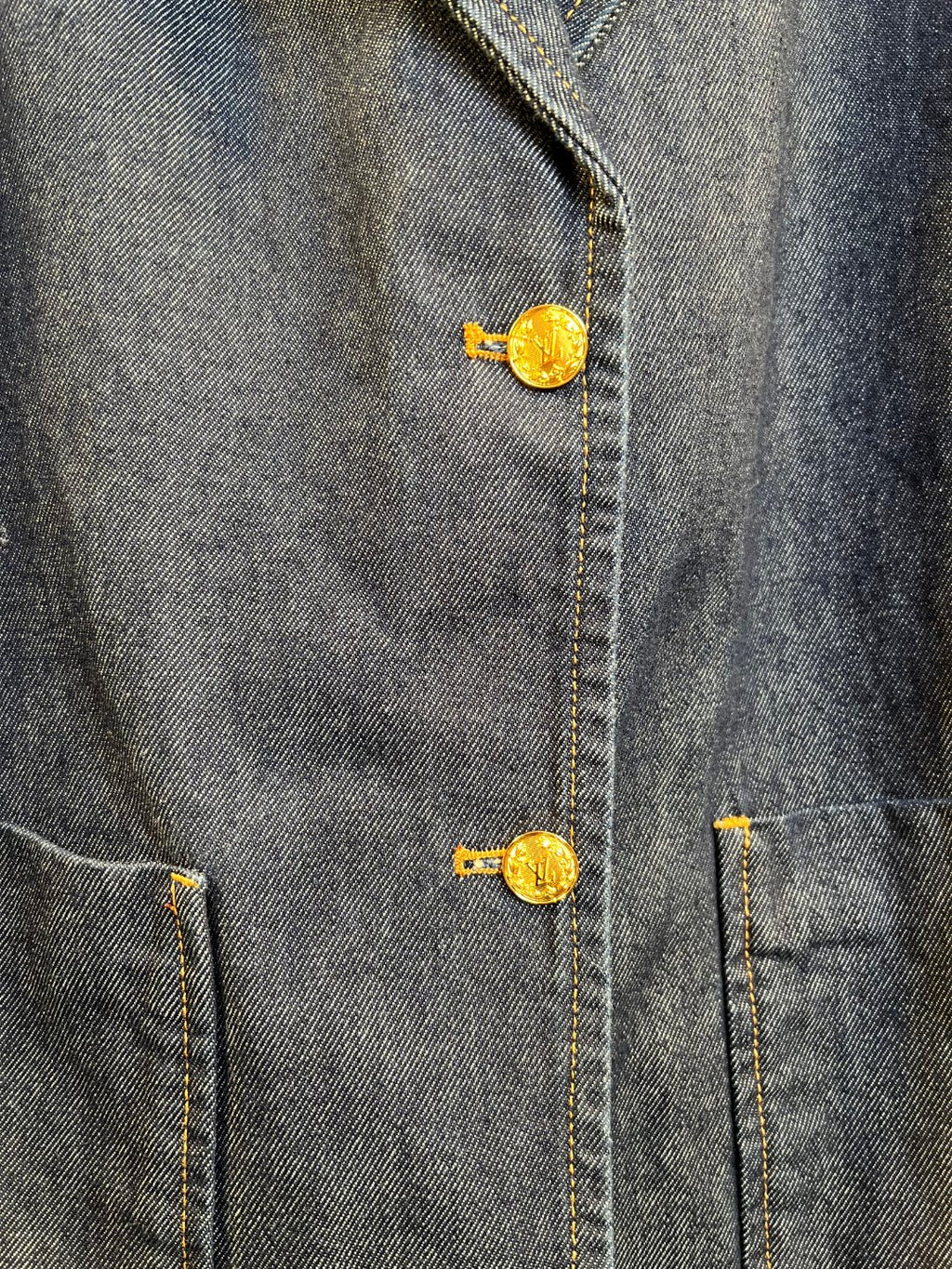 Denim jacket button detail with gold tone metal shank and embroidered emblem