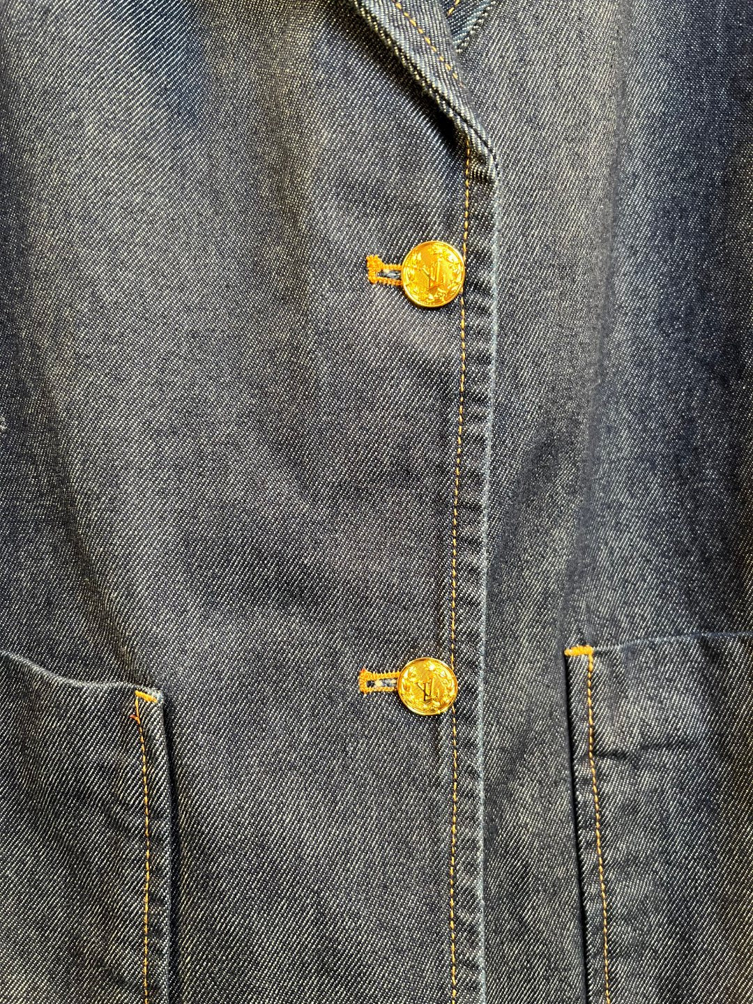 Denim jacket button detail with gold tone metal shank and embroidered emblem