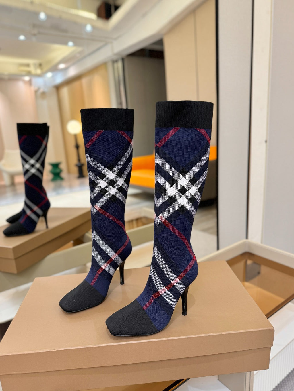 Pair of knee-high knit boots in navy with red and white check pattern and stiletto heels
