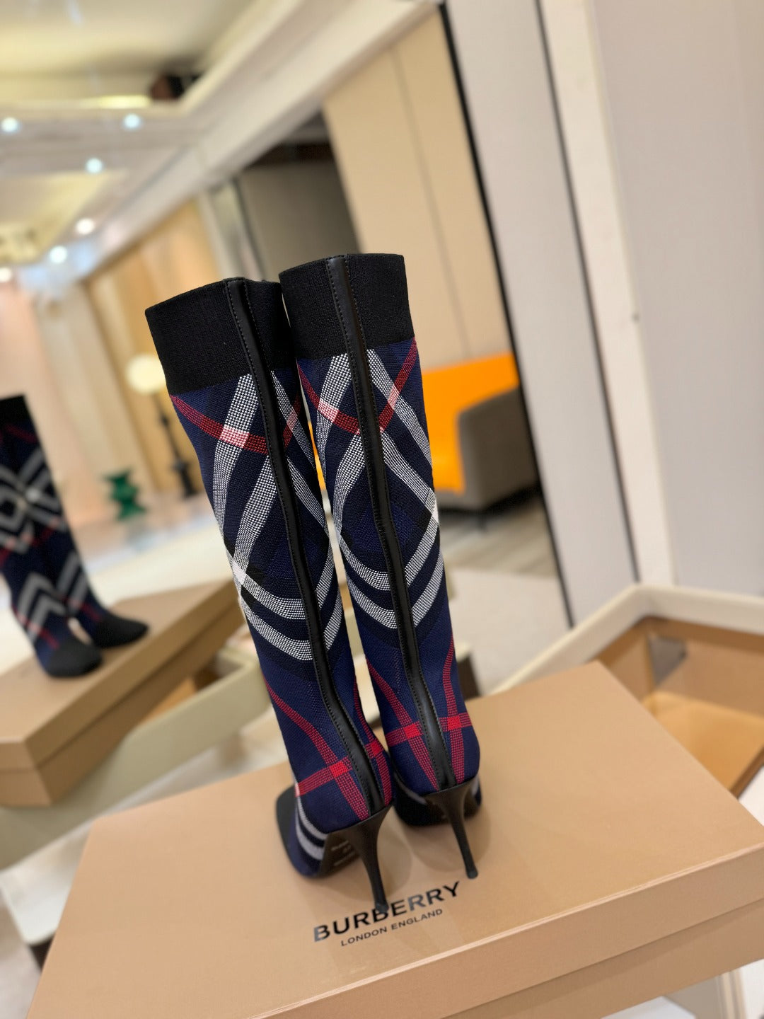 Back view of knee-high knit boots with navy, red, and white check pattern and stiletto heels