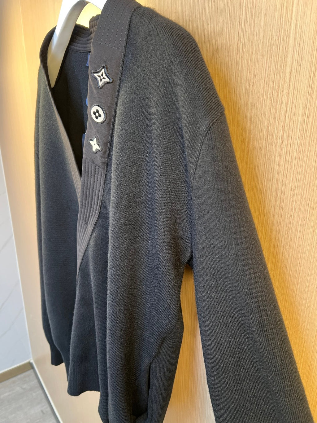 Side view of dark knit sweater with embroidered Louis Vuitton crest patches