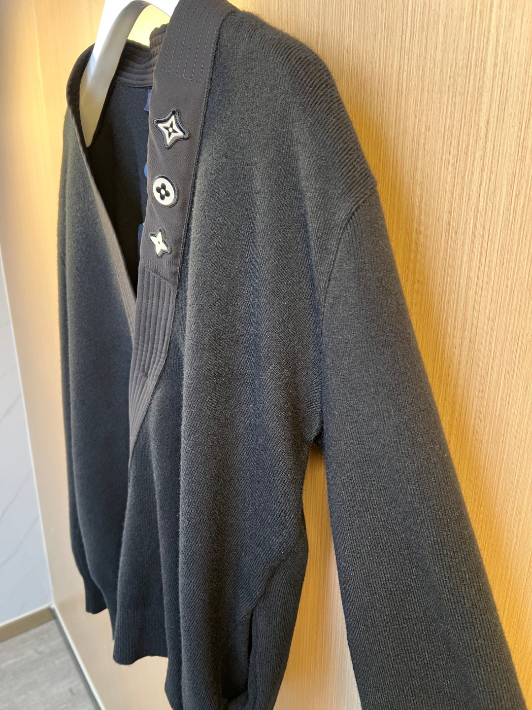 Side view of dark knit sweater with embroidered Louis Vuitton crest patches
