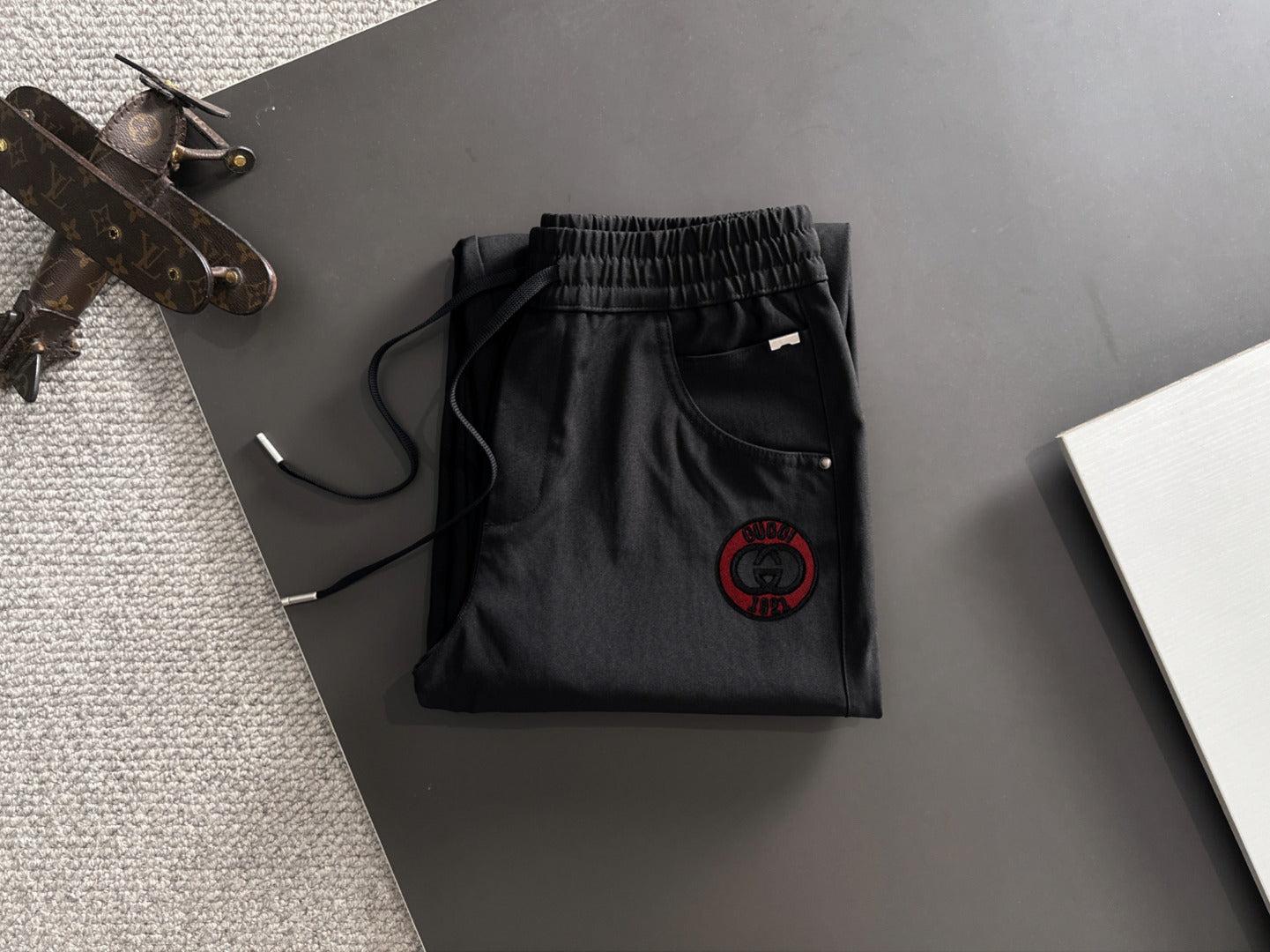 Black Gucci pants folded view with elastic waistband and red logo patch