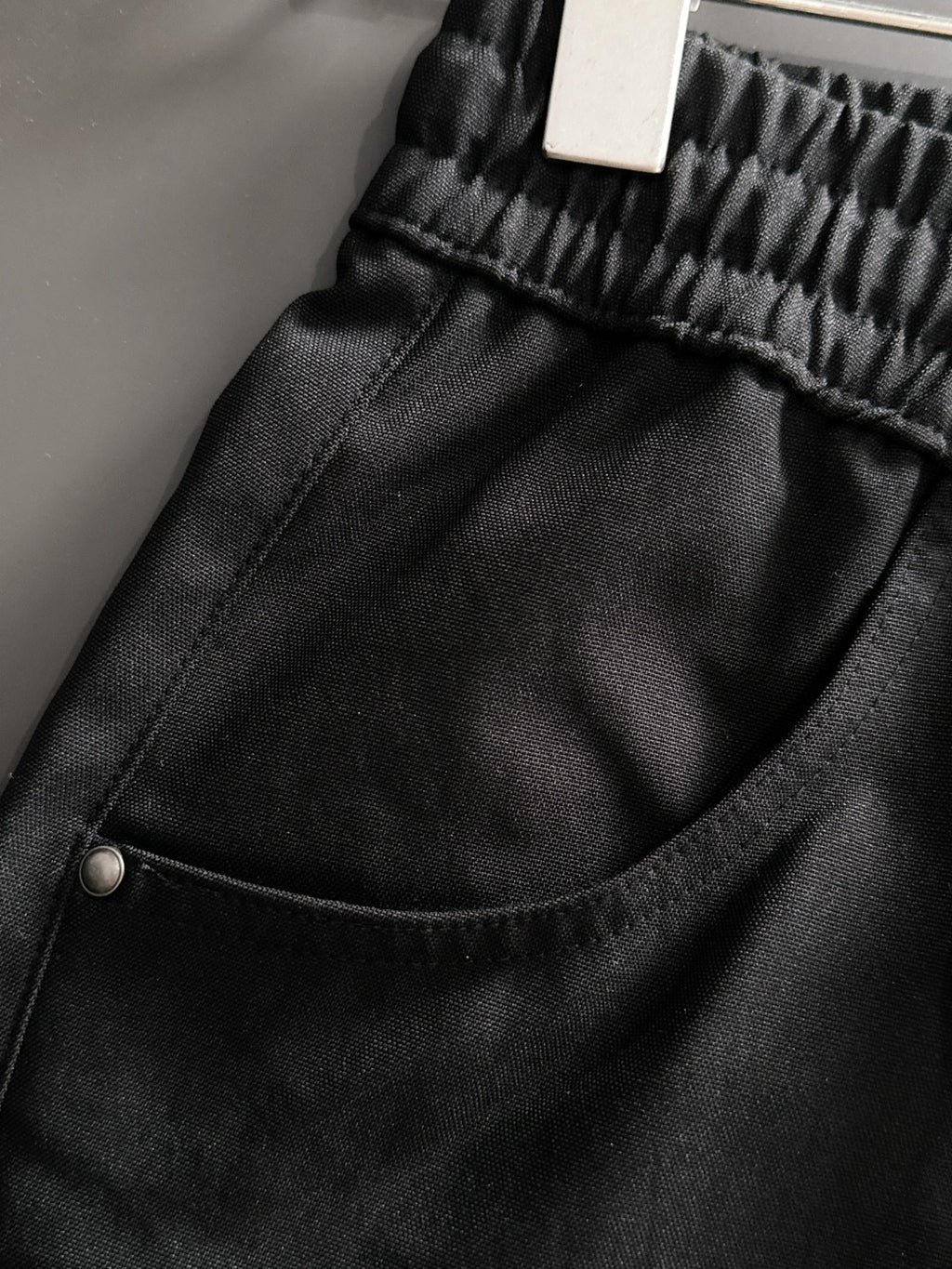Black Gucci pants close-up of curved pocket seam and metal button