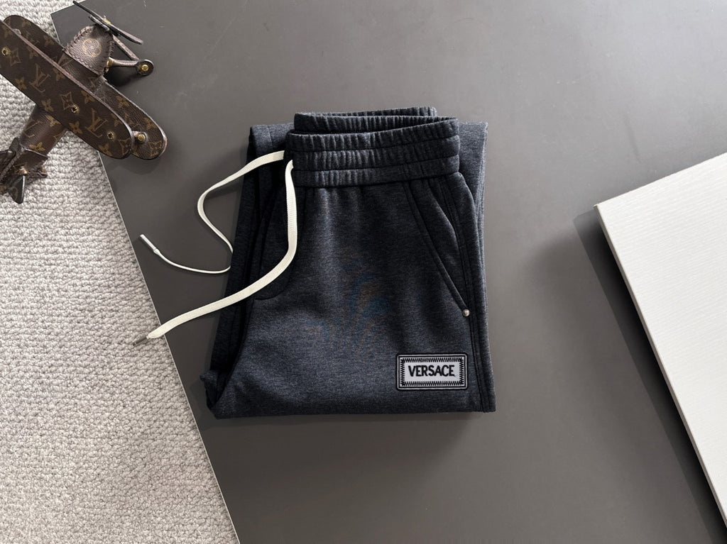 Dark jogger pants with elastic waistband, drawstring, and Versace logo patch