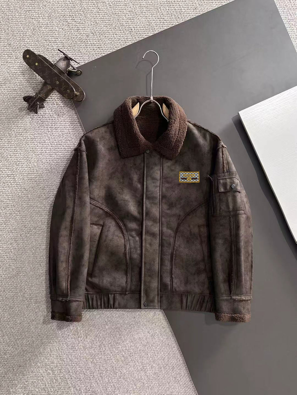 Brown shearling-collar jacket with front zipper and chest logo patch