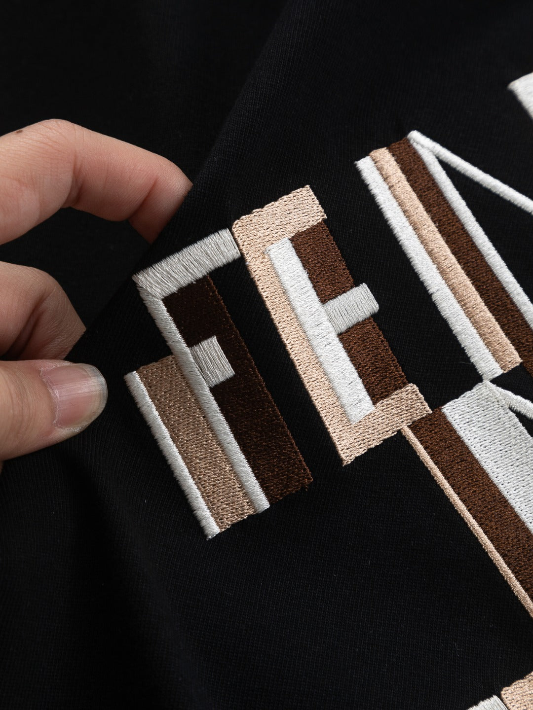 Hand-held close-up of FENDI logo embroidery on black short-sleeve T-shirt