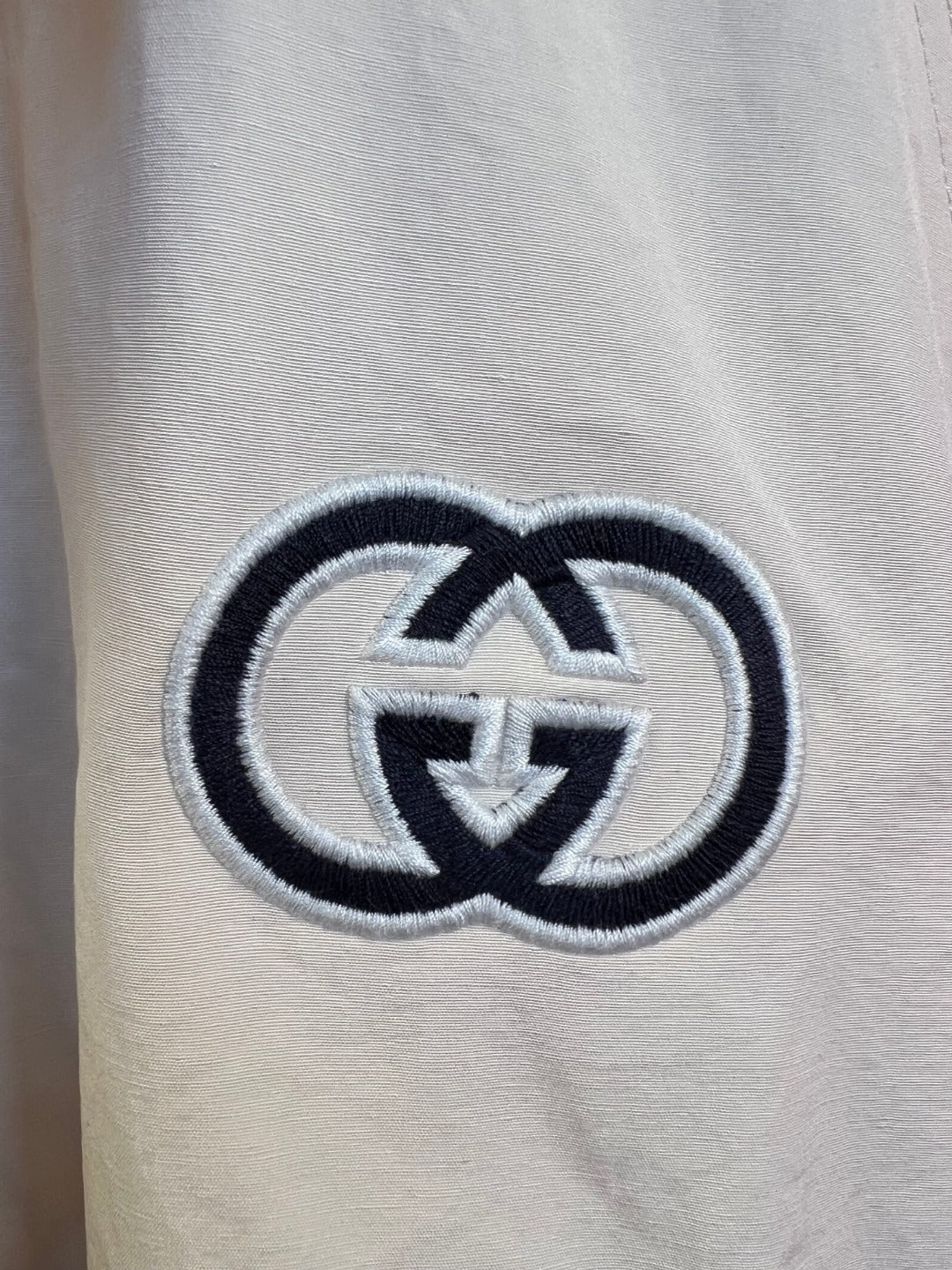 Embroidered logo on light fabric with dark outline and interlocking pattern