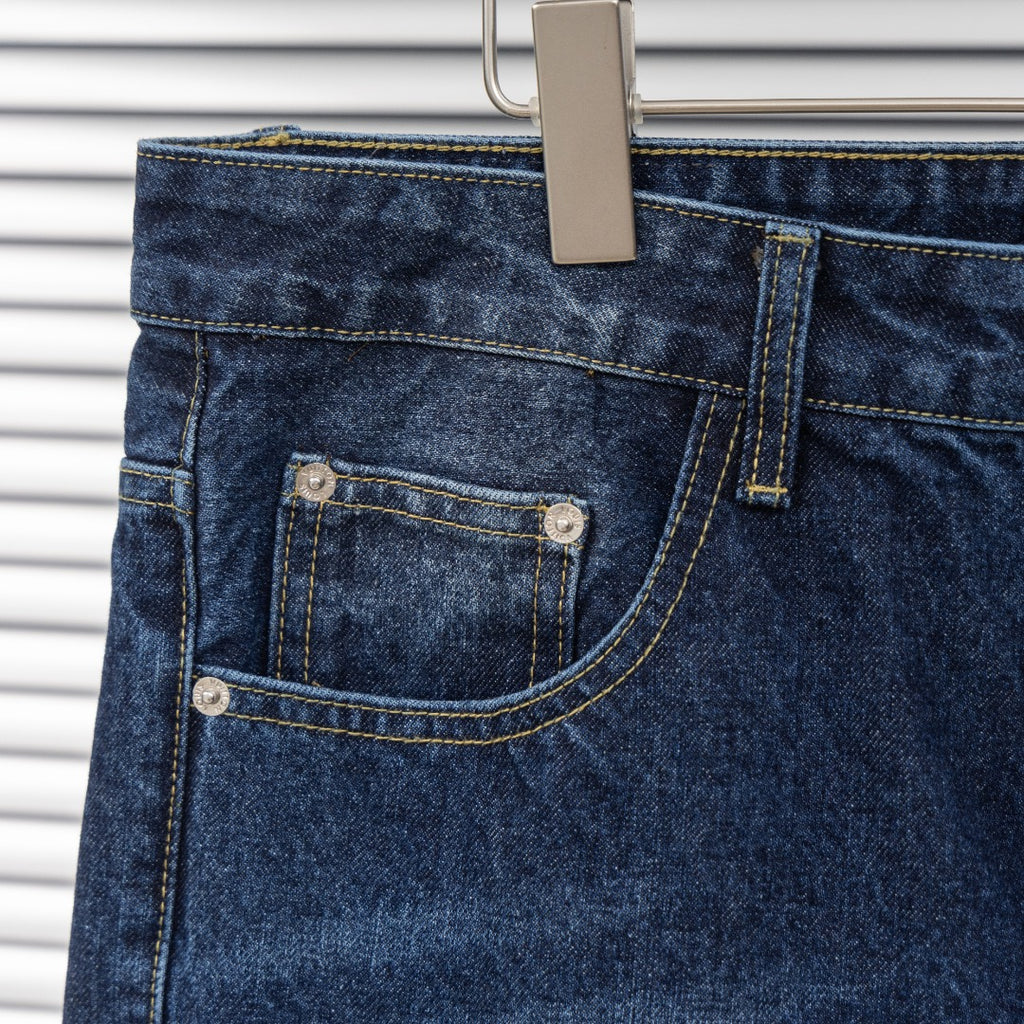 Back pocket of dark blue denim jeans with double-stitched design and metal rivets