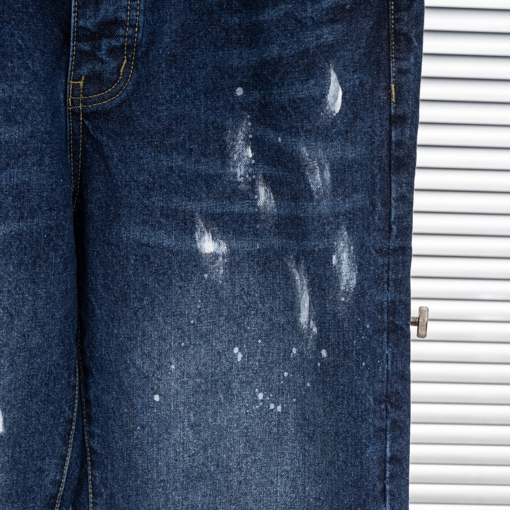 Dark blue denim jeans leg with distressed paint splatter and fading marks