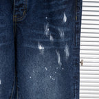 Dark blue denim jeans leg with distressed paint splatter and fading marks