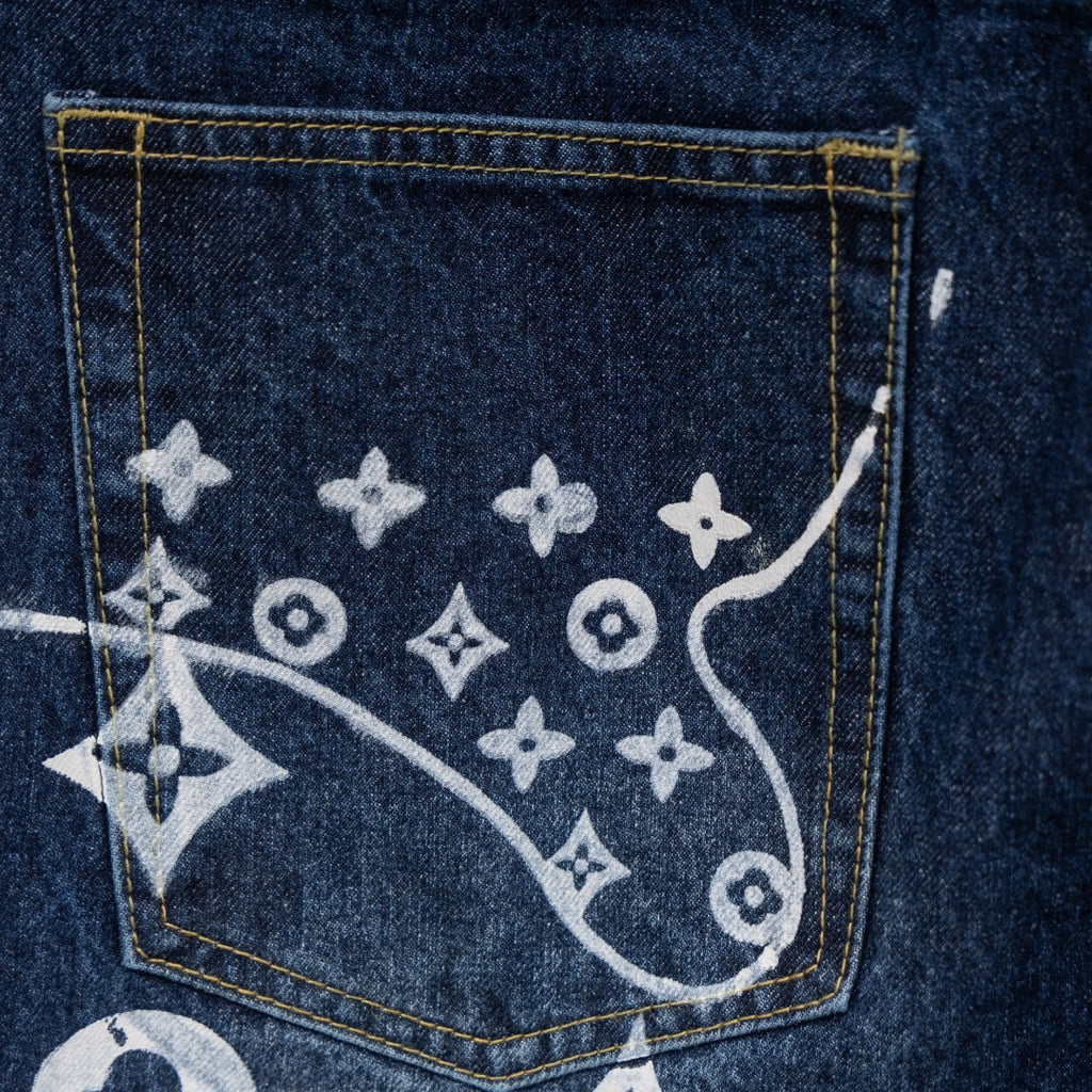 Denim pants back pocket close-up with gold stitching and white monogram print