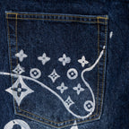 Denim pants back pocket close-up with gold stitching and white monogram print